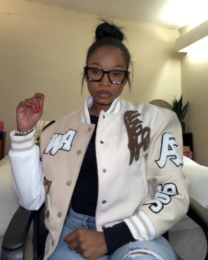 Woman wearing a varsity jacket and glasses, exemplifying a 'hottest' outfit style debate.