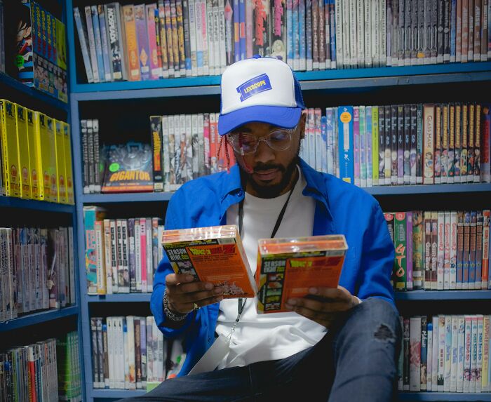 Man in blue jacket and cap reading DVDs in a store aisle, surrounded by shelves of gradually disappeared things.