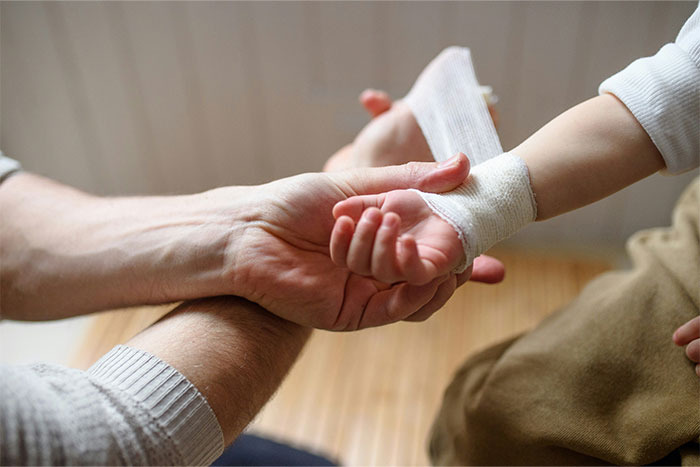 Hands bandaging a child's arm, providing life-saving first aid care in a gentle setting.