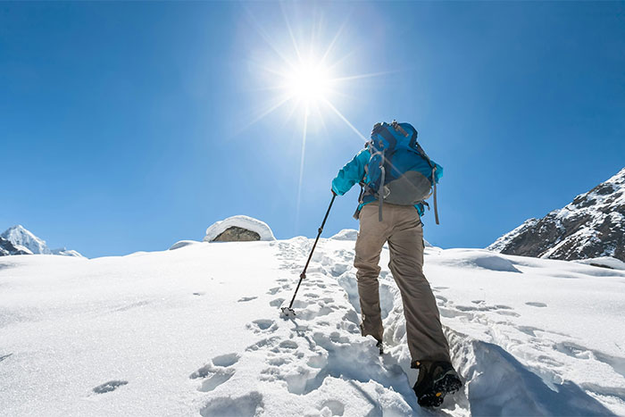Person hiking up a snowy mountain under bright sun, demonstrating life-saving skills in extreme conditions.