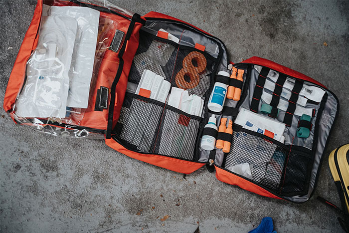 Open first aid kit with emergency supplies neatly organized in red bag on a concrete surface.