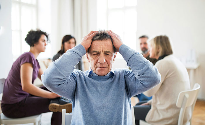 Man in distress holding head, surrounded by people, depicting a need for emergency and first aid assistance.