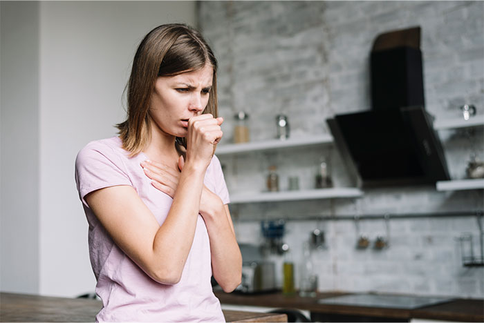 A woman in a kitchen coughing into her hand, representing life-saving tips for emergencies.