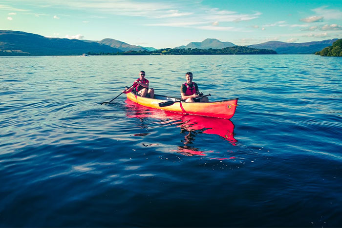 Two individuals in a red kayak on a lake, wearing life vests, highlighting emergency safety tips.