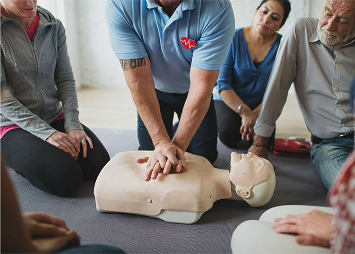 Person demonstrating CPR on a dummy surrounded by onlookers, highlighting emergency and first aid tips.