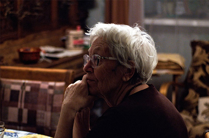 Elderly woman in glasses, deep in thought at a cozy table, illustrating life-saving tips for seniors.
