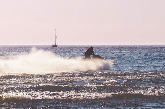 Person jet skiing on the ocean with a sailboat in the background, illustrating life-saving tips.