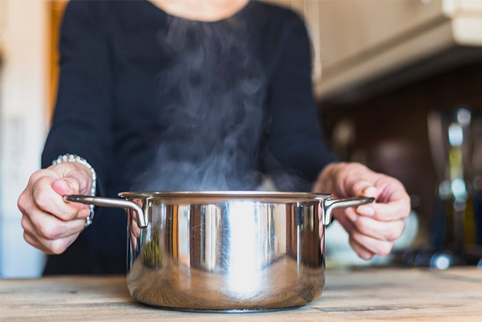 Person in kitchen holding a steaming pot, illustrating a potential emergency first aid scenario.
