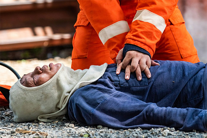 Rescue worker performs CPR on a person lying on gravel, emphasizing life-saving techniques.
