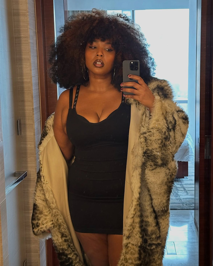 Woman in a fur coat takes a mirror selfie, celebrating body positivity and obesity acceptance.
