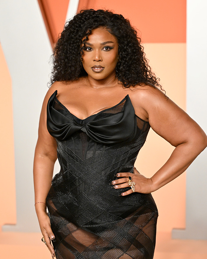 Curly-haired woman in a black dress poses confidently at an event, related to obesity discussion.
