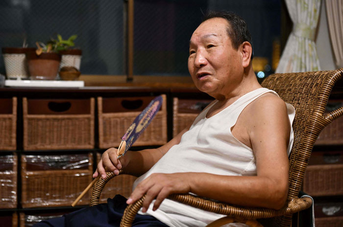 Man sitting in a wicker chair, holding a fan, representing world's longest-serving death row inmate found not guilty.