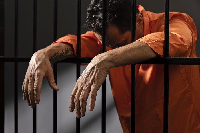 Inmate in orange jumpsuit behind bars, representing longest-serving death row case outcome.