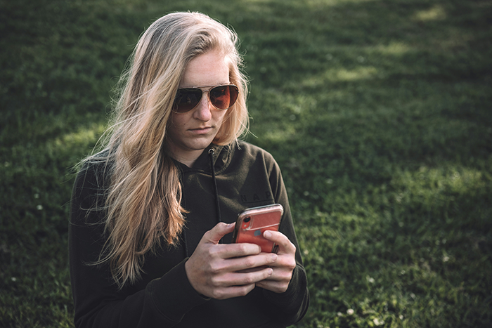 Woman in sunglasses sitting on grass, focused on her phone, amid wedding drama.