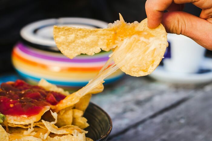Cheesy nacho being lifted from a colorful bowl, symbolizing a snack choice during the worst job interviews.