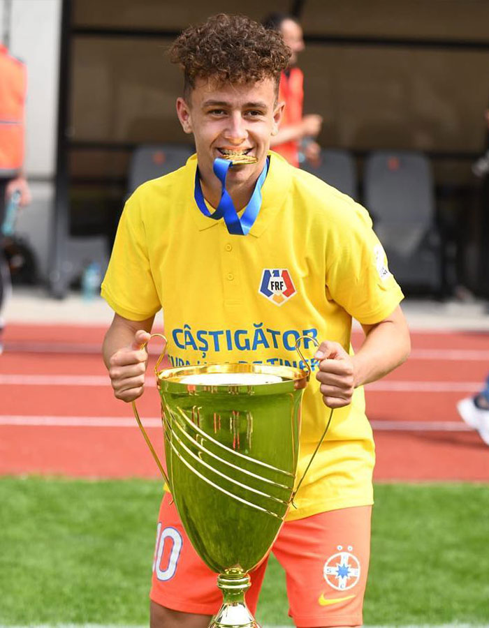 Young footballer holding a trophy, smiling on the field wearing a yellow jersey. Young footballer holding a trophy, smiling on the field wearing a yellow jersey.