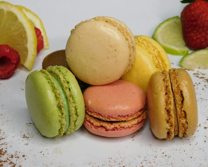 An assortment of colorful macarons on a plate, with sliced fruit in the background, embodying miscellaneous foods.