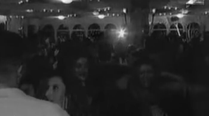 Personas disfrutando en una fiesta con luces tenues; parece una escena normal pero tiene una historia inquietante.