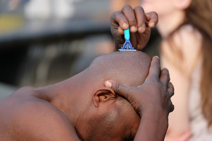 Person shaving their head with a razor outdoors, illustrating the need for inventive grooming solutions.