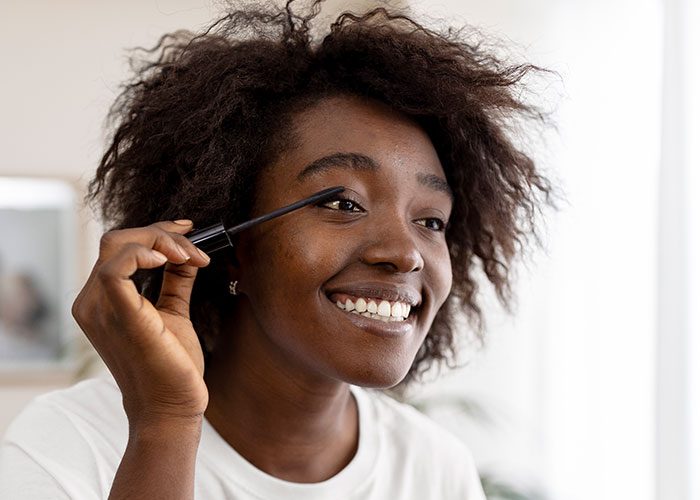 Woman smiling while applying mascara, highlighting coworker's audacity. Woman smiling while applying mascara, highlighting coworker's audacity.
