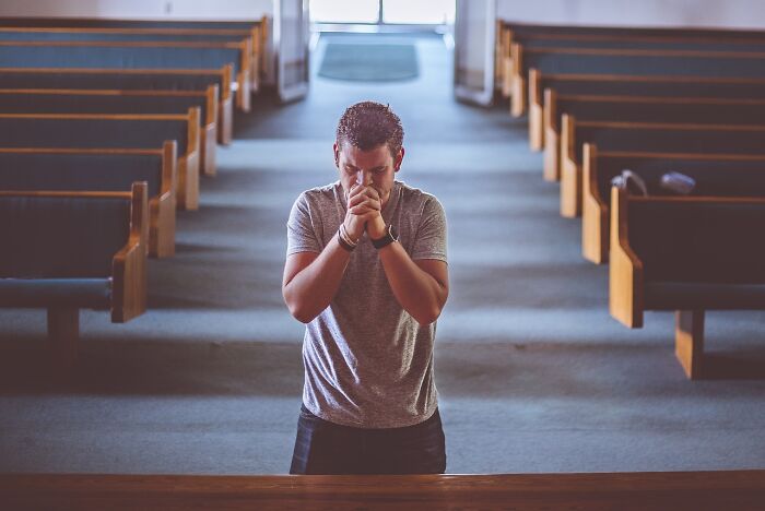 Man deep in thought in a church, contemplating potential scams.
