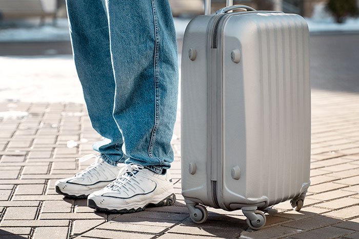 Person in jeans and sneakers standing next to a suitcase, symbolizing mooching scenario.