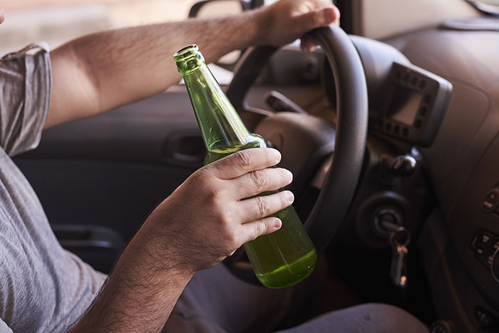 Person holding a green bottle while driving, illustrating a lost license scenario.