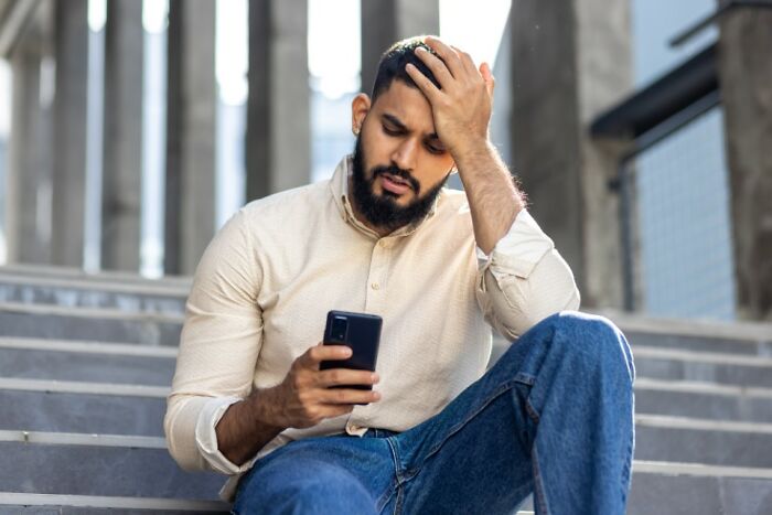 Man sitting on stairs, distressed while looking at phone, reflecting on former best friend.