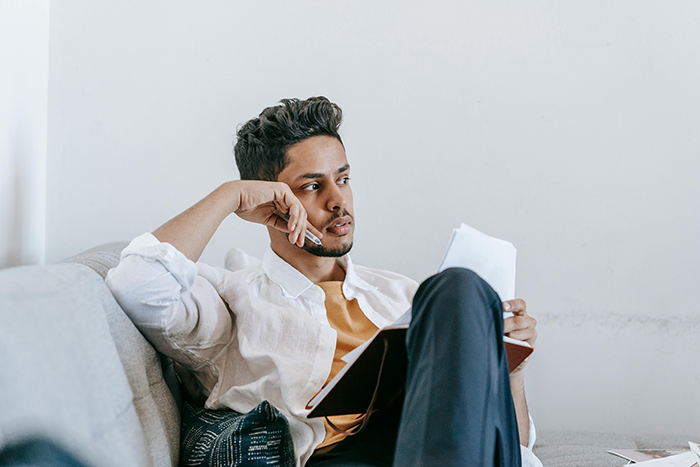 Man sitting on sofa looking thoughtful, holding papers, contemplating end of free rides to work.