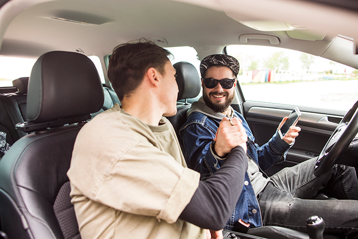 Two friends in a car sharing a handshake, symbolizing the end of free rides to work.