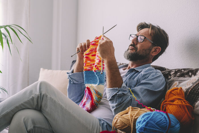 Man knitting colorful yarn on a couch, representing things that get more hate than deserved.