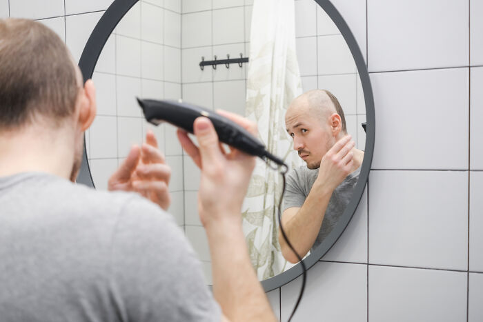 Man using hair clippers, reflecting in the mirror, contemplating inventions yet to be made.
