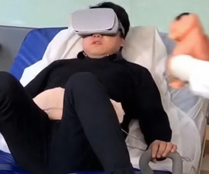 Man in VR headset experiencing childbirth simulation on hospital bed, holding handles. Man in VR headset experiencing childbirth simulation on hospital bed, holding handles.
