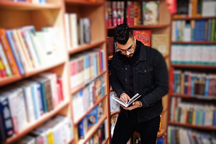 Young man in bookstore reading in the children's section, surrounded by colorful books.