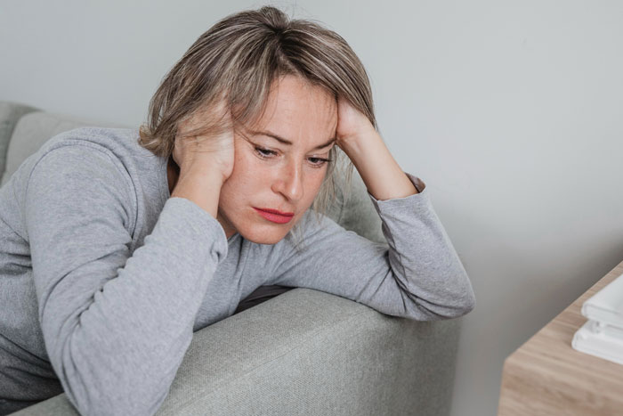 Woman sitting on a couch looking stressed, hands on head, related to financial stress and borrowing issues. Woman sitting on a couch looking stressed, hands on head, related to financial stress and borrowing issues.
