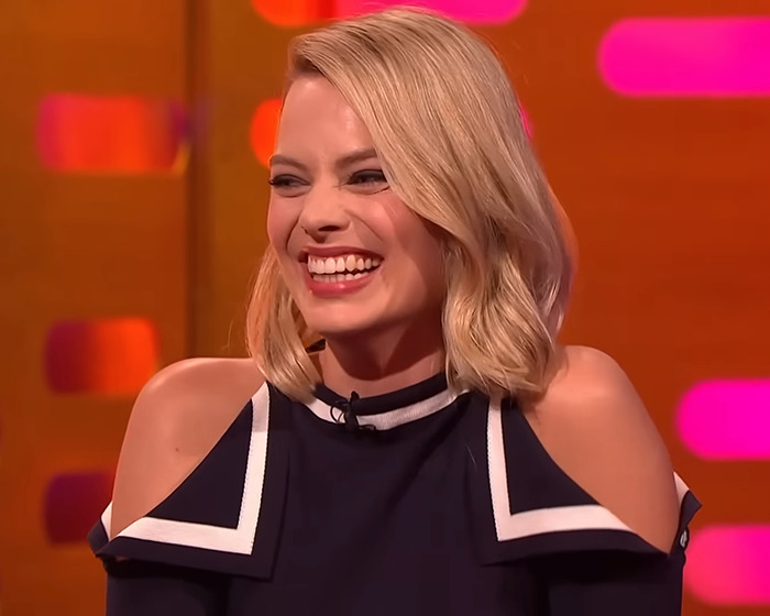 Smiling woman in a black and white top on a talk show set, associated with Wuthering Heights costume news.