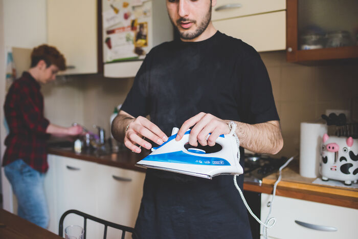 Un hombre en la cocina sosteniendo la plancha de manera descuidada, ejemplificando a parejas consideradas "idiotas".