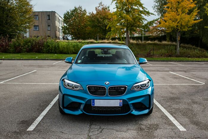 Blue BMW parked in empty lot with autumn trees in background, cloudy day. Worst job interviews setting.
