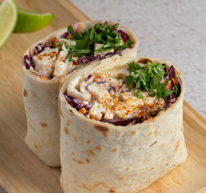 Two delicious wrap sandwiches filled with chicken, vegetables, and herbs on a wooden board.