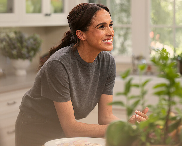 Meghan Markle smiling in a kitchen setting, surrounded by greenery and decor. Meghan Markle smiling in a kitchen setting, surrounded by greenery and decor.