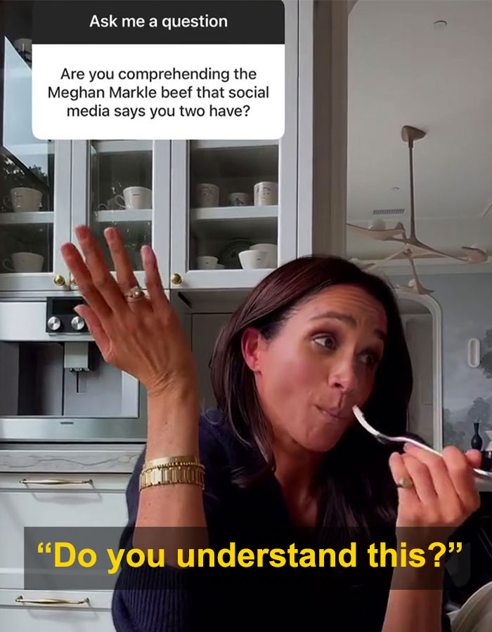 Woman in kitchen responding to question about Meghan Markle feud rumors, looking curious and holding a spoon.