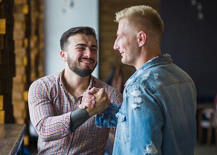 Two men shake hands warmly in a casual setting, smiling and engaging positively.