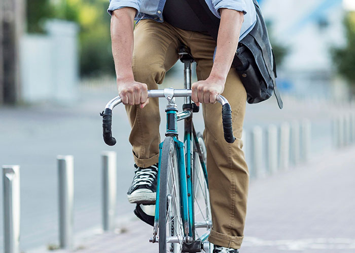 Man riding a bicycle on an urban street, wearing brown pants and black sneakers.