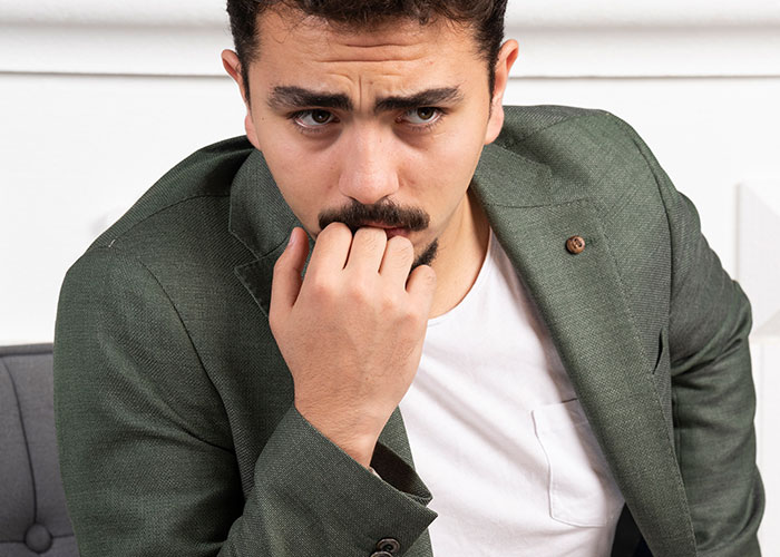 Man in a thoughtful pose wearing a green blazer, looking pensive and seated indoors.