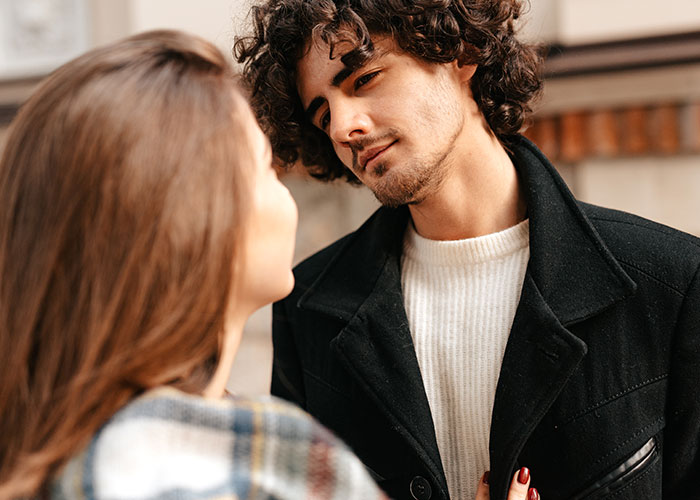 A man in a black coat looking intently at a woman, showcasing curiosity in a conversation setting.