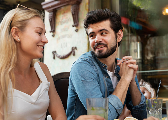 A man in a blue shirt and a woman in a white top smiling at an outdoor café.
