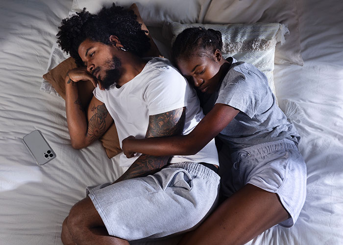 Couple lying in bed, with woman hugging man from behind, exploring questions about men and relationships.