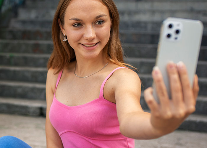 Woman in a pink tank top sitting on stairs, taking a selfie with smartphone, thinking about questions about men.