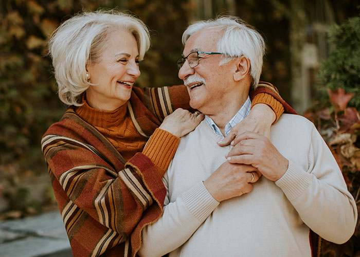 Elderly couple smiling and embracing outdoors, woman in a striped shawl, showcasing joyful companionship and connection.