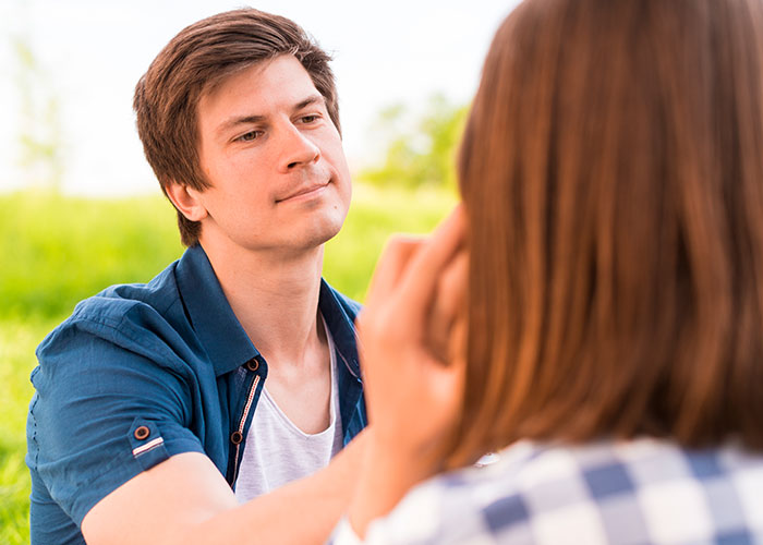 Man in a blue shirt looking at a woman outdoors, discussing questions about men in a serene setting.